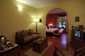 A hotel room with a sofa, a bed, a television, a lamp, and a view through an archway. - Pride Sun Village Resort (Arpora)