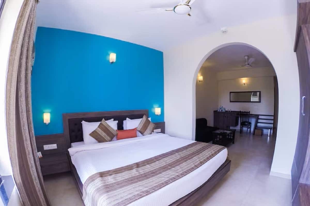 A hotel room with a large bed, a ceiling fan, and a view of the dining area through an archway.