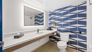 A bathroom with a white sink, mirror, and toilet, with geometric patterned tiles on the walls. - Best Western Plus Lower South End (Charlotte)