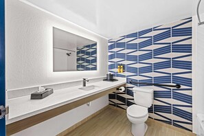 A bathroom with a white sink, mirror, and toilet, with geometric patterned tiles on the walls. - Best Western Plus Lower South End (Charlotte)