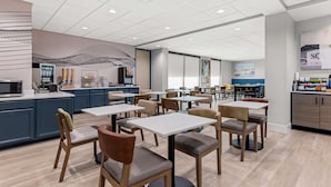 A modern dining area with tables and chairs, a kitchen counter, and a wall with a geometric design. - Best Western Plus Lower South End (Charlotte)