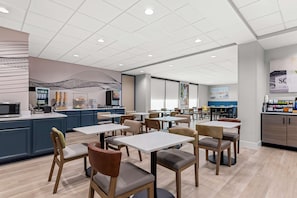 A modern dining area with tables and chairs, a kitchen counter, and a wall with a geometric design. - Best Western Plus Lower South End (Charlotte)