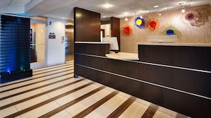 En hotellobby med modern design, inklusive en receptionsdisk, en glashiss och ett mönstrat golv.