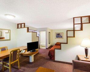 A hotel room with a wooden desk, a television, a sofa, a lamp, and a staircase. - Rodeway Inn & Suites Fiesta Park (San Antonio)