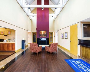 A hotel lobby with a fireplace, two patterned armchairs, a reception desk, and a blue mat with 'Rodeo Inn & Suites' text. - Rodeway Inn & Suites Fiesta Park (San Antonio)