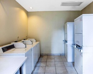 A laundry room with stacked washing machines and dryers, a control panel, and a tiled floor. - Rodeway Inn & Suites Fiesta Park (San Antonio)
