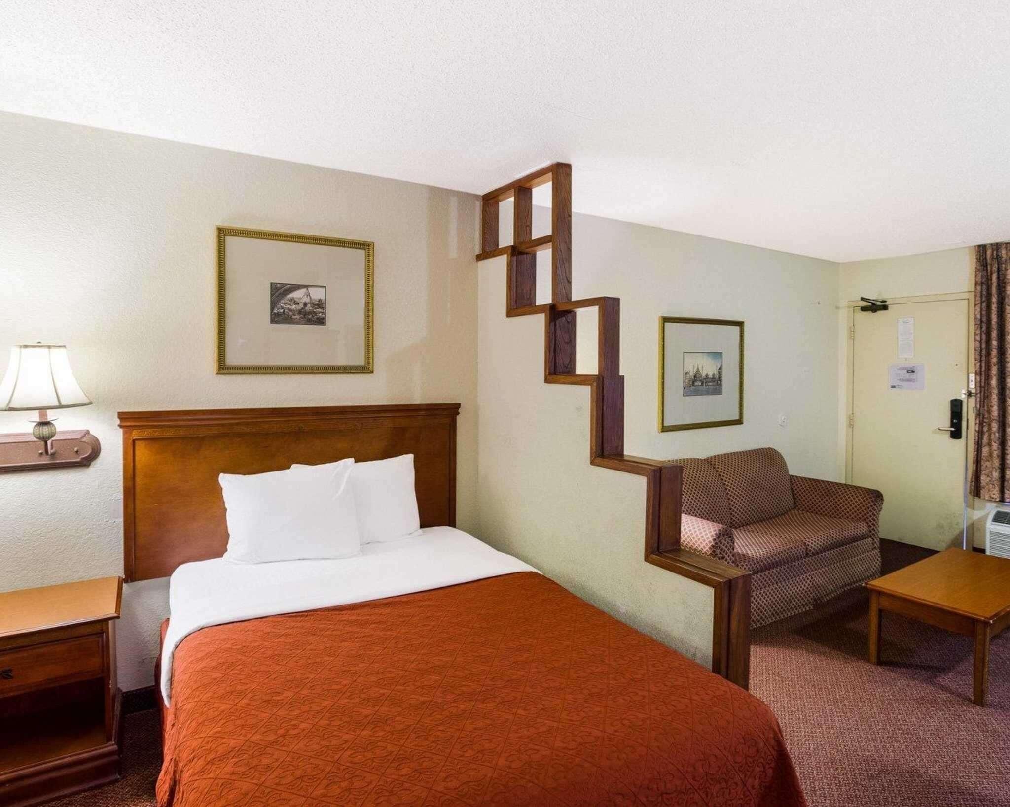 A hotel room with a bed, a chair, a desk, and a nightstand.