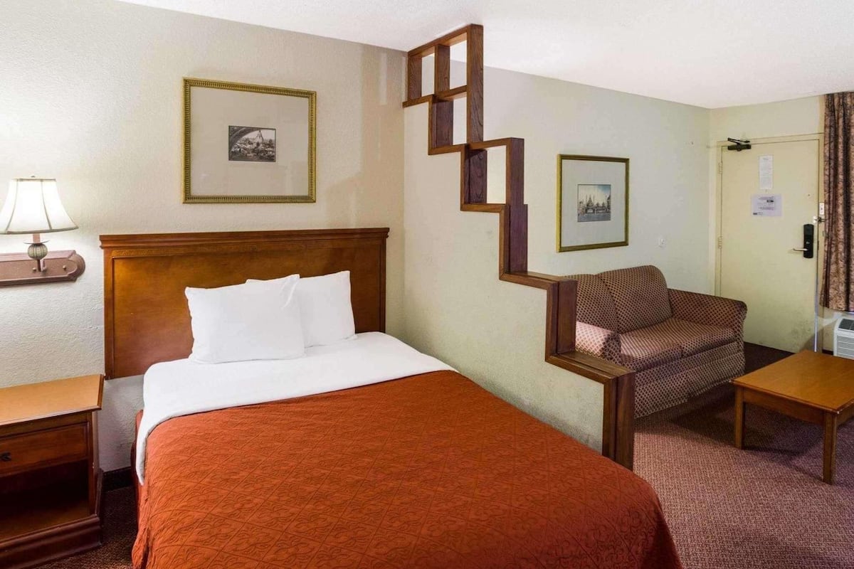 A hotel room with a bed, a chair, a desk, and a nightstand.