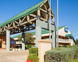 A hotel with a covered parking area, a sign indicating it's a Rodeway Inn & Suites, and a building with a green roof. - Rodeway Inn & Suites Fiesta Park (San Antonio)