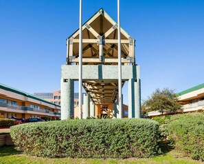A building with a central atrium, multiple floors, and a surrounding hedge. - Rodeway Inn & Suites Fiesta Park (San Antonio)