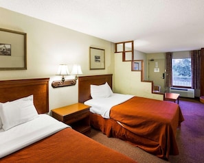A hotel room with two beds, a nightstand with lamps, a mirror, and a window with curtains. - Rodeway Inn & Suites Fiesta Park (San Antonio)