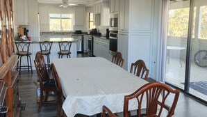Een ruime eethoek met een lange tafel en houten stoelen, een keuken met witte kasten, en een grote schuifdeur die leidt naar een buitenruimte.