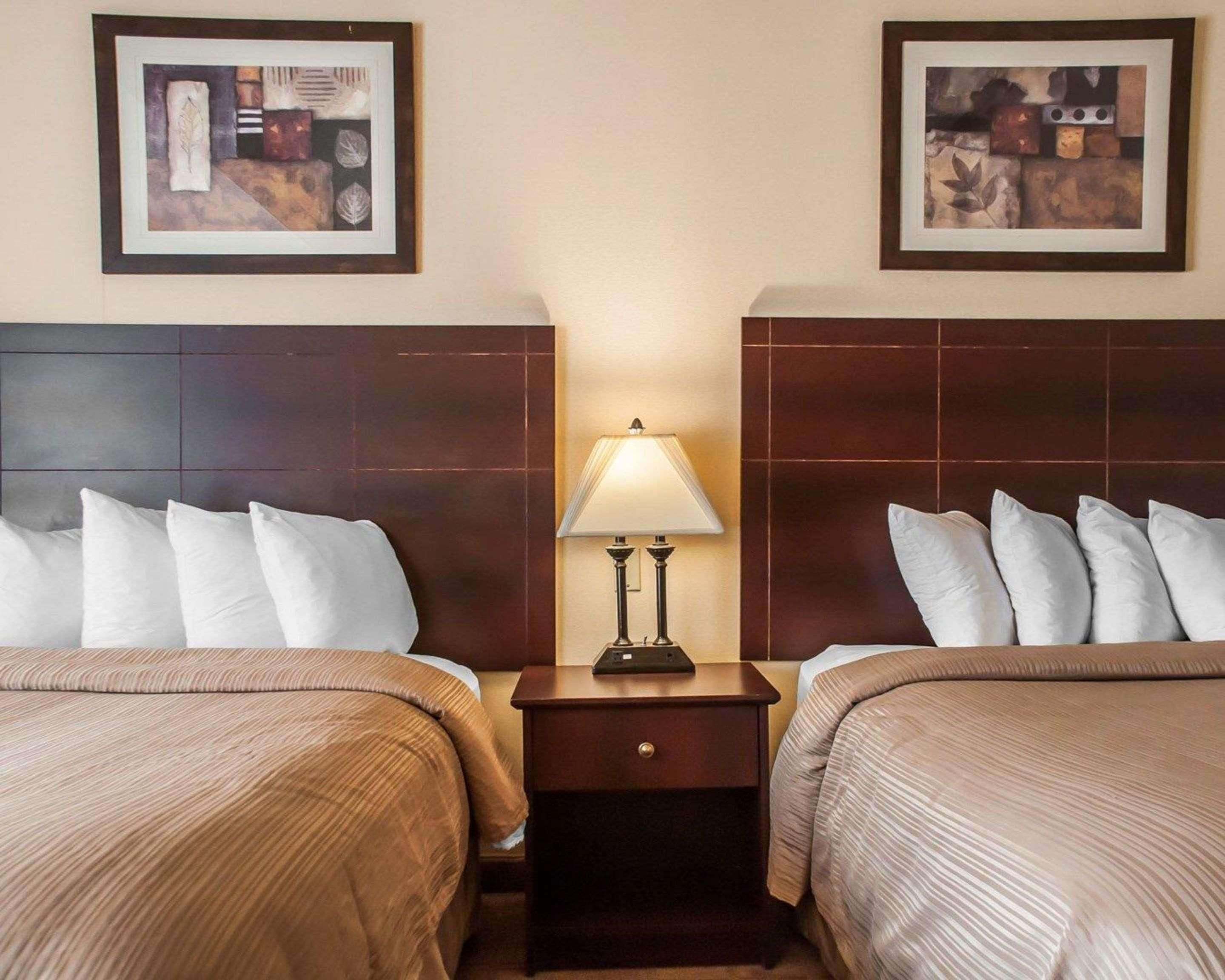 Habitació d'hotel amb dos llits, una tauleta de nit amb una làmpada i dues obres d'art emmarcades a les parets.