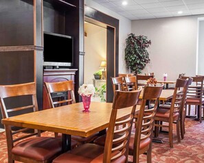 A hotel dining area with wooden tables and chairs, a television, and a potted plant. - Quality Inn Airport Buffalo (Buffalo)