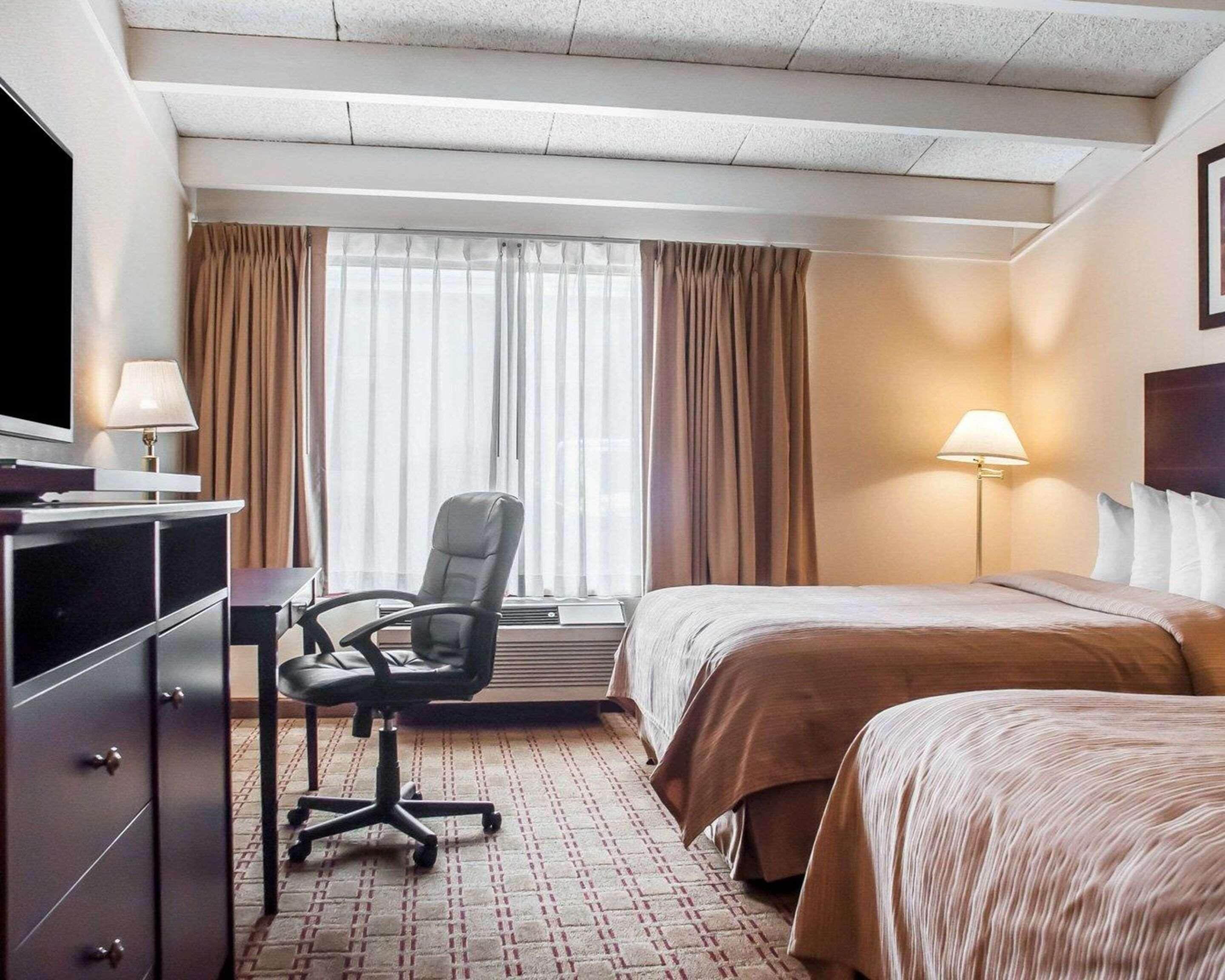 A hotel room with a bed, a desk with a chair, a television, and a window with curtains.