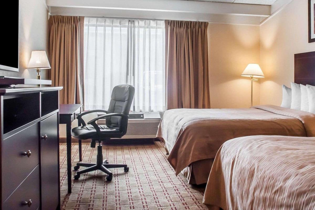 A hotel room with a bed, a desk with a chair, a television, and a window with curtains.