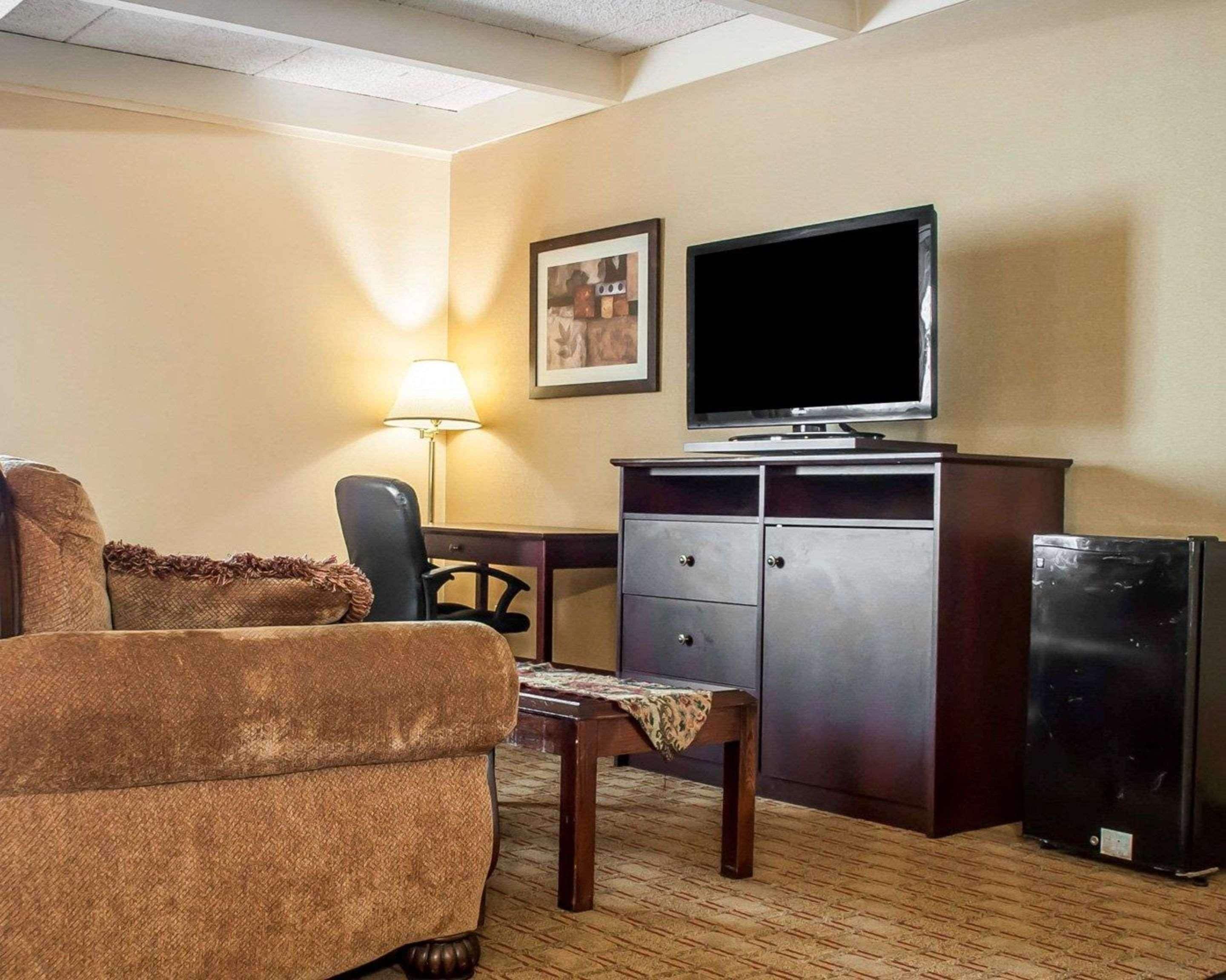 A hotel room with a sofa, a desk, a television, a lamp, and a refrigerator.