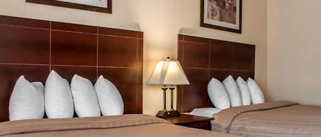 Ein Hotelzimmer mit zwei Betten, einem Nachttisch mit Lampe und zwei gerahmten Bildern an den Wänden.