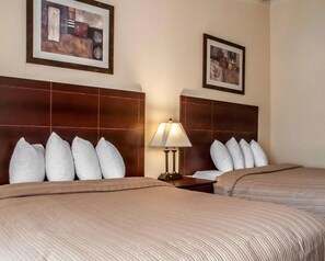 A hotel room with two beds, a nightstand with a lamp, and two framed pictures on the walls. - Quality Inn Airport Buffalo (Buffalo)