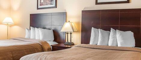 A hotel room with two beds, a headboard, a nightstand with a lamp, and two framed pictures on the wall.