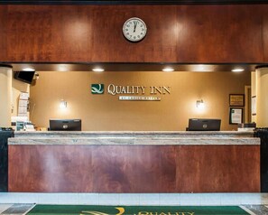 A reception desk with a clock, a sign reading 'Quality Inn by Choice Hotels,' and two laptops on the counter. - Quality Inn Airport Buffalo (Buffalo)