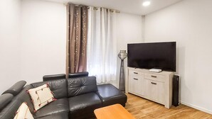 Una sala de estar con un sofá de cuero negro, una mesa de centro de madera, un televisor sobre un mueble bajo y una lámpara de pie alta.