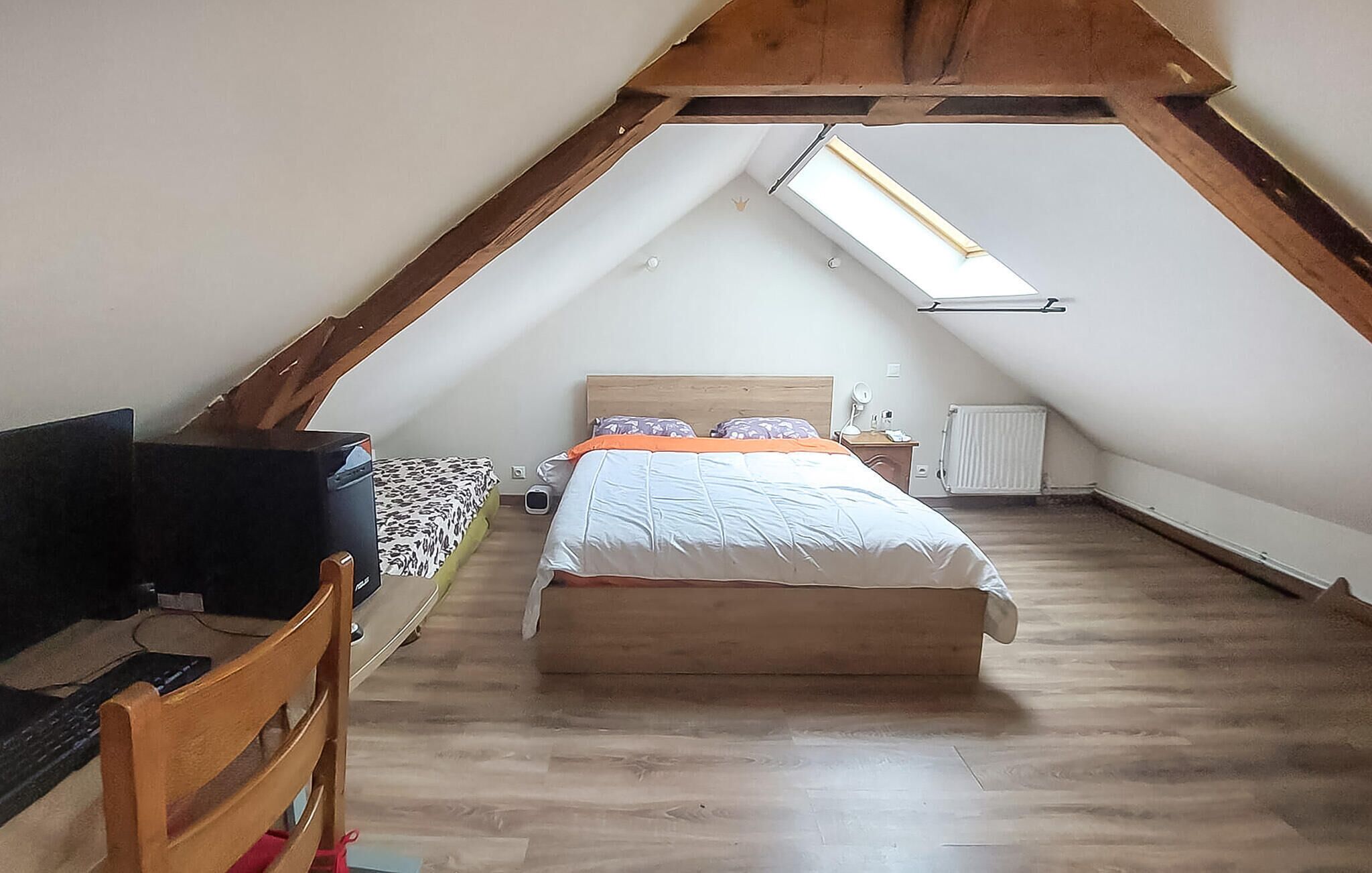 Un dormitorio con techo inclinado, cama, escritorio y silla.
