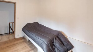 Una habitación pequeña con cama individual, suelo de madera, pared blanca y puerta con marco de madera.