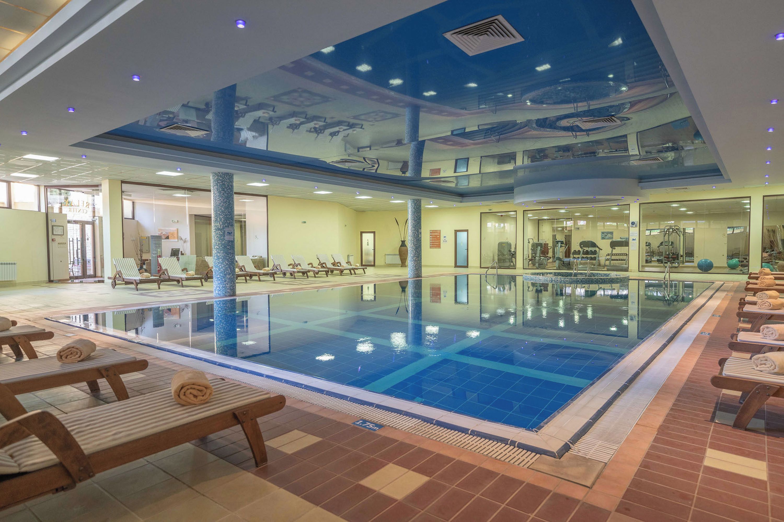 An indoor swimming pool with multiple lanes, sun loungers, and a ceiling mural.