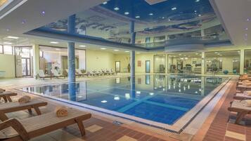 An indoor swimming pool with multiple lanes, sun loungers, and a ceiling mural.