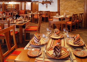 A restaurant with wooden tables and chairs, each set with plates, glasses, and napkins. - Grifid Hotel Bolero (Varna)