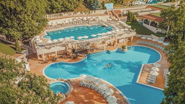 An aerial view of a resort with multiple swimming pools, sun loungers, and a large building with a pool deck. - Grifid Hotel Bolero (Varna)