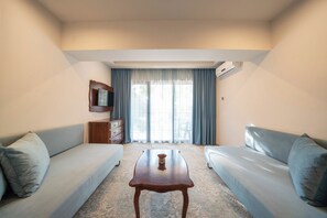 A hotel room with a sofa set, a small table, a television mounted on the wall, and a window with curtains. - Grifid Hotel Bolero (Varna)