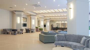 Um hall amplo com um sofá modular cinzento grande, uma mesa de centro redonda e uma área de estar com cadeiras e uma pequena mesa.