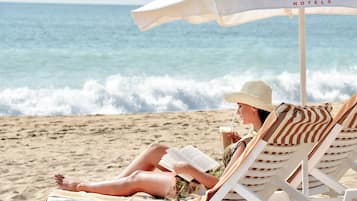 A beach scene with a person reading under a Grifid Hotels umbrella.