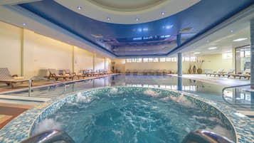 Piscina interior com borda azulejada, espreguiçadeiras e teto com iluminação embutida.