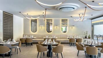 Interior moderno de restaurante com mesas redondas, cadeiras bege e uma área central de estar com um banco acolchoado.