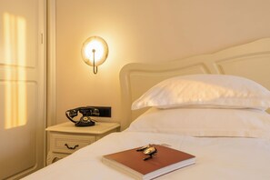 A hotel room with a bed, a nightstand with a rotary phone, a wall-mounted light, and a window with blinds. - Grifid Hotel Bolero (Varna)