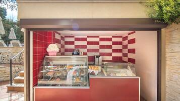 A food kiosk with a checkered red and white tile wall, a glass display case with pastries, and a small counter with a coffee machine.