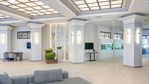 A spacious lobby with a grey sofa, a round table, and a large TV screen. - Grifid Hotel Bolero (Varna)