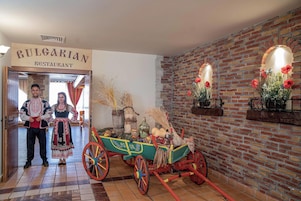 Interior de un restaurante búlgaro tradicional con una pared de ladrillo rústica, un carro de madera con adornos y un letrero sobre la entrada.