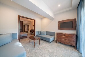 A modern living room with a sofa, a coffee table, a TV mounted on the wall, and a wooden dresser. - Grifid Hotel Bolero (Varna)