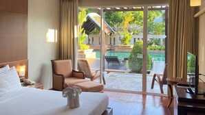 A hotel room with a bed, a chair, a desk, a TV, and a sliding glass door leading to a pool area. - Mission Hills Phuket Golf Resort & Spa (Wichit)
