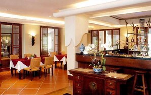 A dining area with wooden furniture, a bar with a display of bottles, and a decorative vase with flowers. - Mission Hills Phuket Golf Resort & Spa (Wichit)