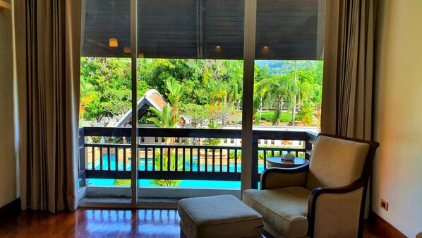 A room with a view of a pool and greenery, a chair, and a small table. - Mission Hills Phuket Golf Resort & Spa (Wichit)