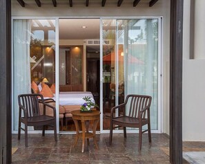 A room with a bed, two chairs, a small table, and a sliding glass door leading to a balcony. - Mission Hills Phuket Golf Resort & Spa (Wichit)