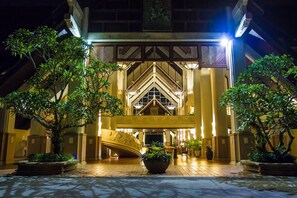Una entrada de hotel con un gran arco, una escalera central y plantas en macetas.