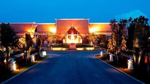 A hotel entrance with a central building, a road leading to it, and well-lit pathways.