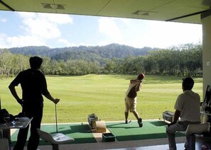 Un campo da golf con vista sulle montagne, un golfista nell'atto di colpire la palla e un caddie nelle vicinanze.