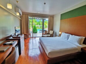 A hotel room with a bed, desk, chair, and a view of a pool and greenery. - Mission Hills Phuket Golf Resort & Spa (Wichit)